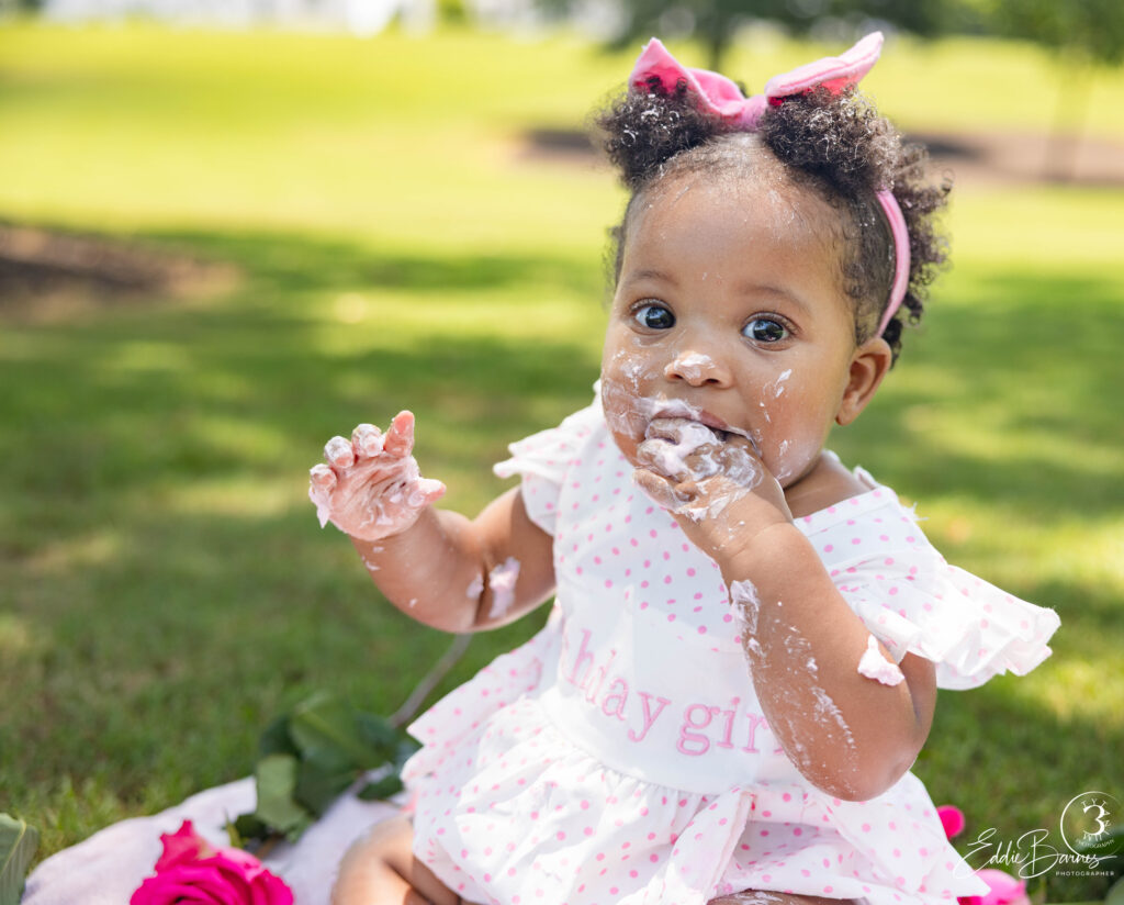 Baby girl with frosting on face eating cake during luxury portrait photography cake smash session in Greenville SC.