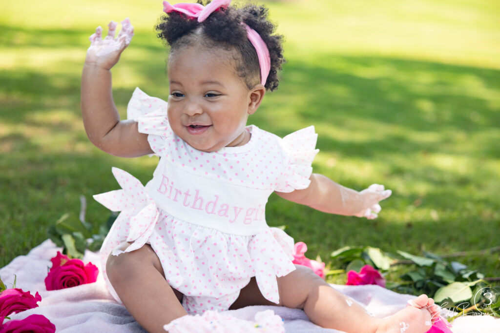 One-year-old baby girl sitting on a blanket in Simpsonville SC park for luxury portrait photography.