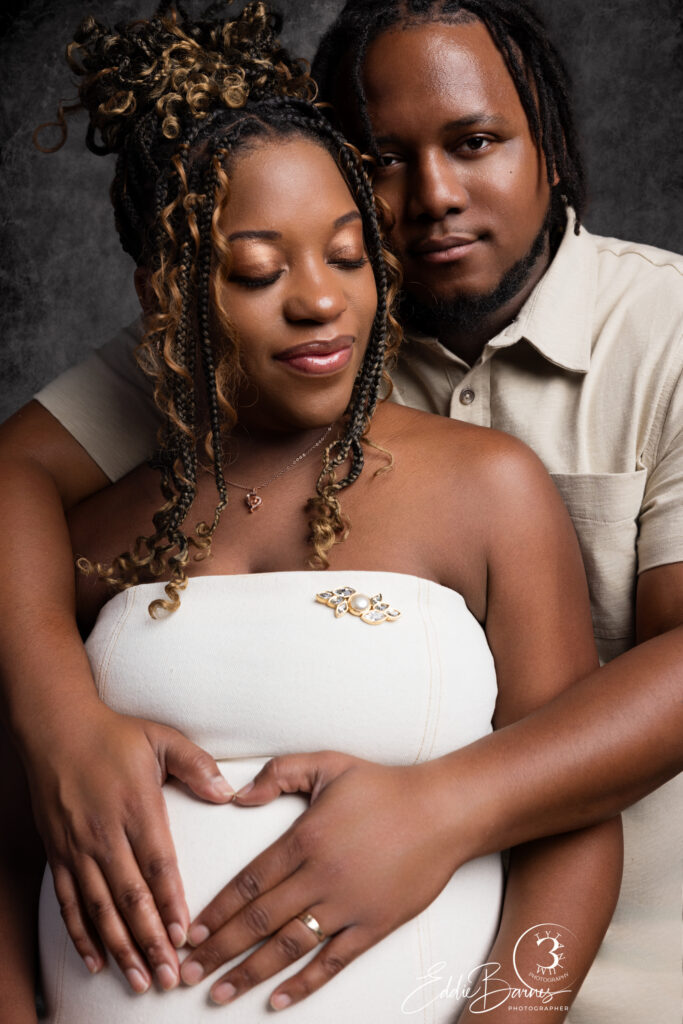 Expecting couple in elegant maternity portrait with hands on mother’s belly