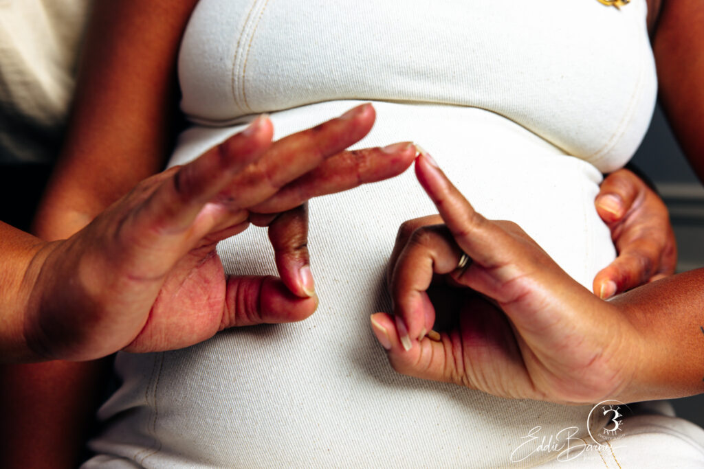 Close-up of couple’s hands forming a heart on mother’s belly during maternity session