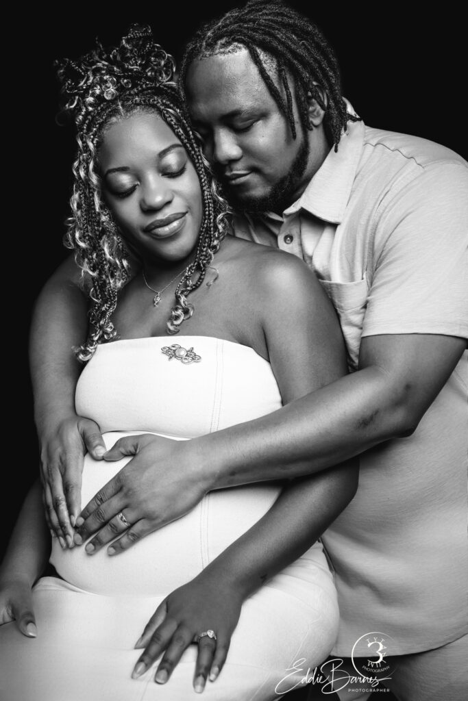 Expecting couple in black and white maternity portrait, father embracing mother’s belly tenderly